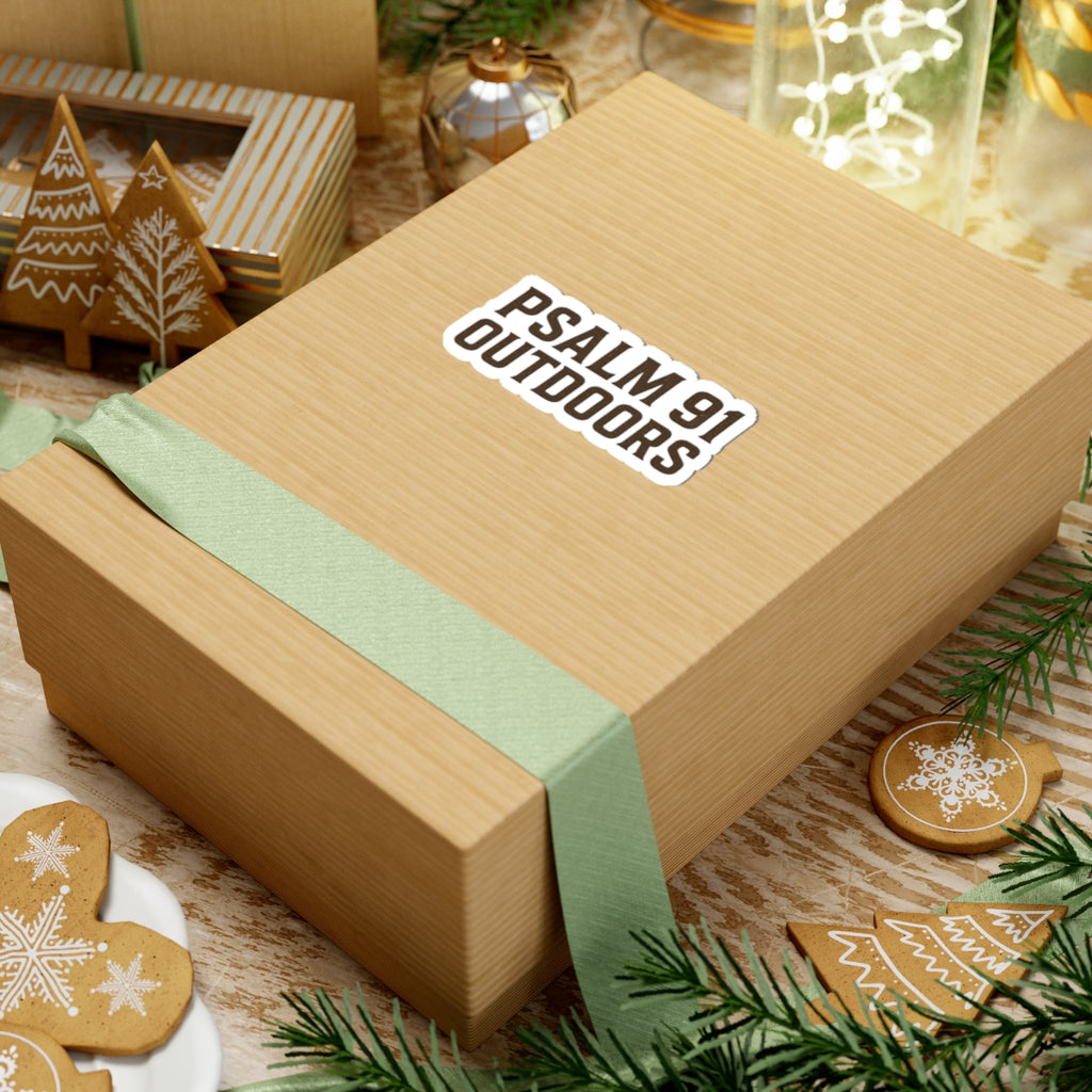 Gift box with a green ribbon and 'Psalm 91 Outdoors' label, surrounded by Christmas-themed cookies and decorations.